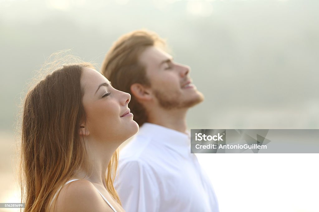 Couple of man and woman breathing deep fresh air Profile of a couple of man and woman breathing deep fresh air together at sunset Breathing Exercise Stock Photo