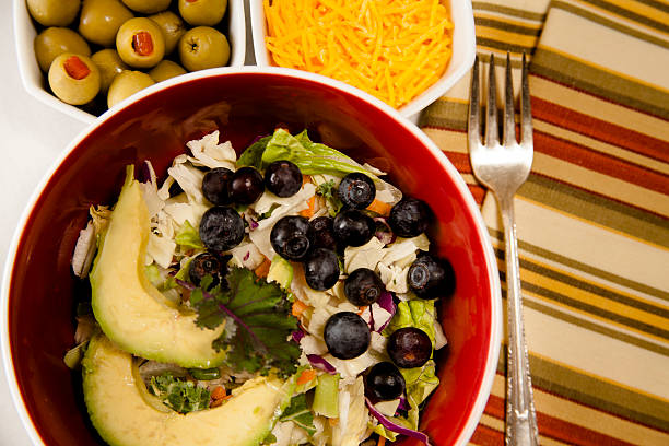 istock Mixed greens salad in bowl. Olives, cheese, fork, napkin. 516285048