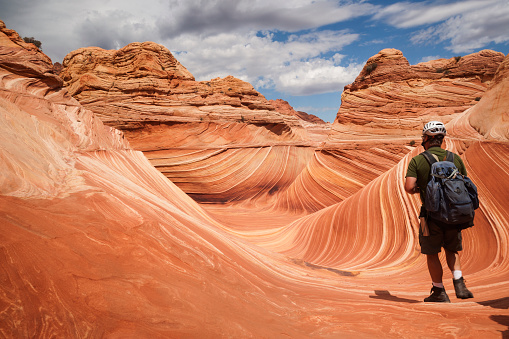 Backpacker exploring the reddish colored  sandstone mountain at the Wave, a striated rock formation in Coyote Butte, Page, Arizona, USA
