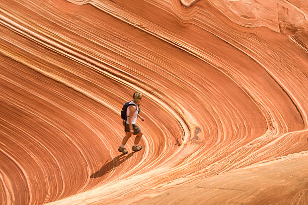 Woman hikes up a striated rock Caucasian woman in 30s to 40s hikes up a striated rock formation in Coyote Butte called The Wave, Page, Arizona the wave arizona stock pictures, royalty-free photos & images