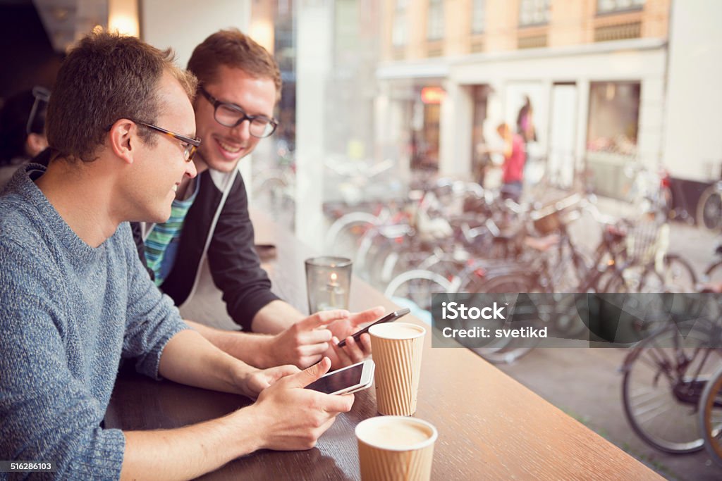 Friends at cafe. Friends drinking coffee and using smart phones at cafe in city centre. Denmark, Copenhagen. Coffee - Drink Stock Photo