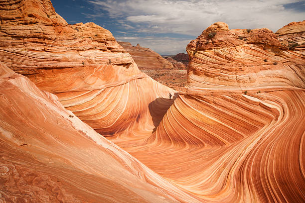 Lone hiker explores the Wave in American Southwest Hiker in distanace exploring the reddish colored  sandstone mountain at the Wave, a striated rock formation in Coyote Butte, Page, Arizona, USA coyote buttes stock pictures, royalty-free photos & images