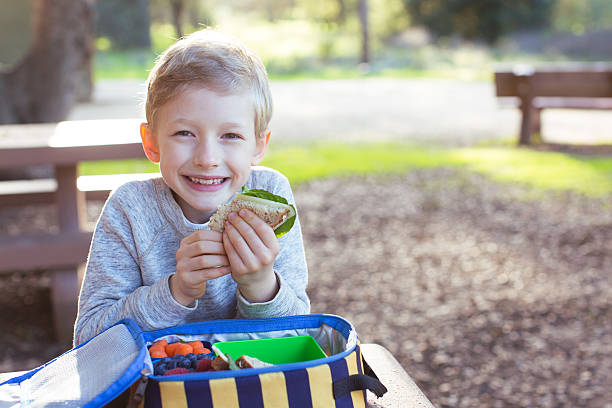 kid at school lunch smiling schoolboy enjoying recess and healthy lunch food elementary student healthy eating schoolboy stock pictures, royalty-free photos & images