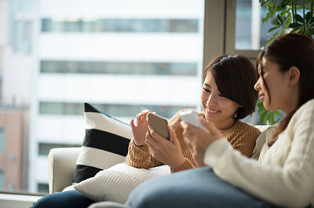 les femmes qui ont vu amis et smartphone sur canapé - digital tablet women enjoyment happiness photos et images de collection