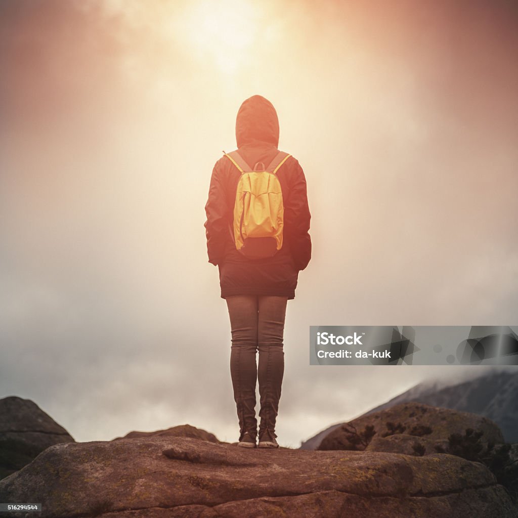 Traveler with backpack walking in mountains at sunset Traveler with backpack walking in a misty mountains at sunset. Stock photo. Adult Stock Photo