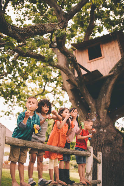 bambino divertirsi con gli amici nel parco che soffia bollicine - playground schoolyard playful playing foto e immagini stock