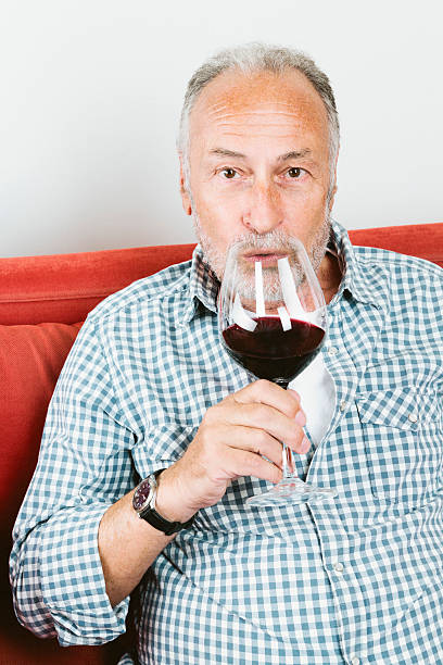 istock Senior man sitting on couch drinking red wine 516314731