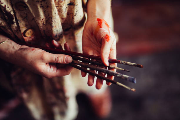 Hands of an artist wearing a traditional smock holding paintbrus Cropped shot of the hands of a woman artist holding a few well-used paintbrushes and wearing a messy paint-covered traditional artist's smock bristle stock pictures, royalty-free photos & images