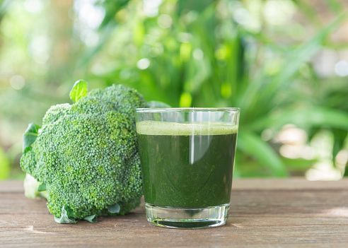 Glass of broccoli juice placed on a wooden table.