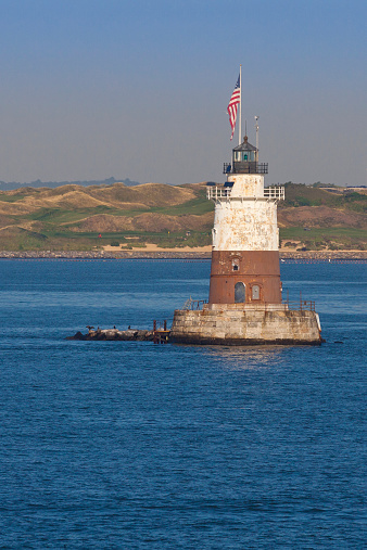 Robbins Reef Light, with Bayonne Golf Course in background, Bayonne, NJ, USA. The image lit by early morning sun. The Robbins Reef Light Station is a sparkplug lighthouse located off Constable Hook in Bayonne, along the west side of Main Channel, Upper New York Bay. The tower and integral keepers quarters were built in 1883.