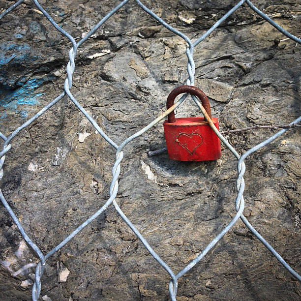 Hearth shaped symbol scratched onto a red padlock. It is locked onto a wire mesh used to contain the rocky wall from crumbling down