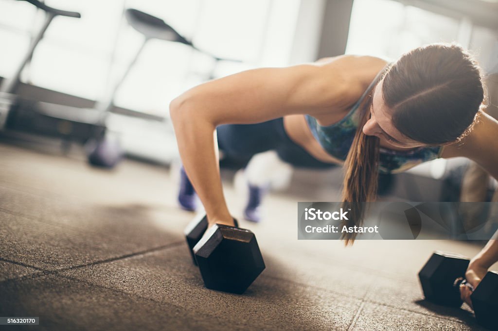 Gym Woman doing push-up exercise with dumbbell. Strong female doing fitness workout. Active Lifestyle Stock Photo