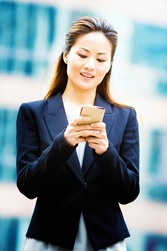 Young Asian female office worker text messaging outdoors.