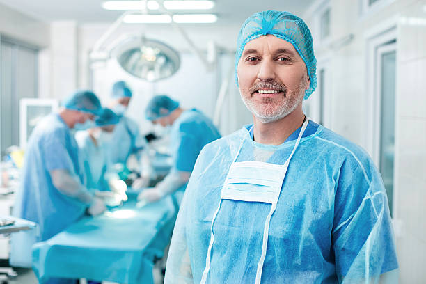 Cheerful old surgeon is examining the operation This operation is going well. Portrait of senior male doctor standing and smiling in surgery. The surgeons are operating with concentration on background surgeon stock pictures, royalty-free photos & images