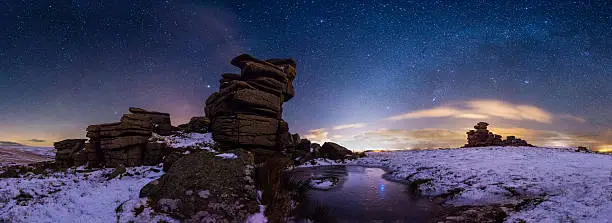 A snow covered Great Staple Tor under a starry night sky taken at Dartmoor National Park.