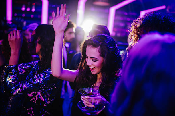 Young woman dancing in a club with a cocktail Happy young adult woman dancing with her friends in a night club holding a cocktail in hand dance floor stock pictures, royalty-free photos & images