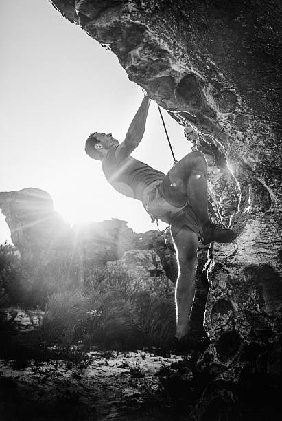 Climbing man hanging on rope in rock as he climbs the boulder. Black and white with sunflare.