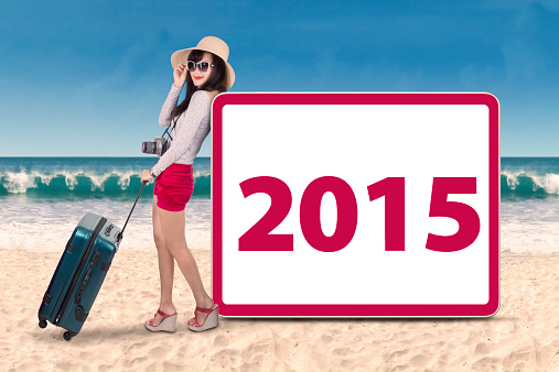 Female holding bag on beach and leans to a board with number 2015