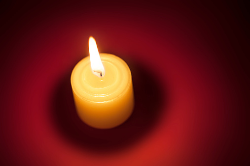 Top view of burning candle on red background.