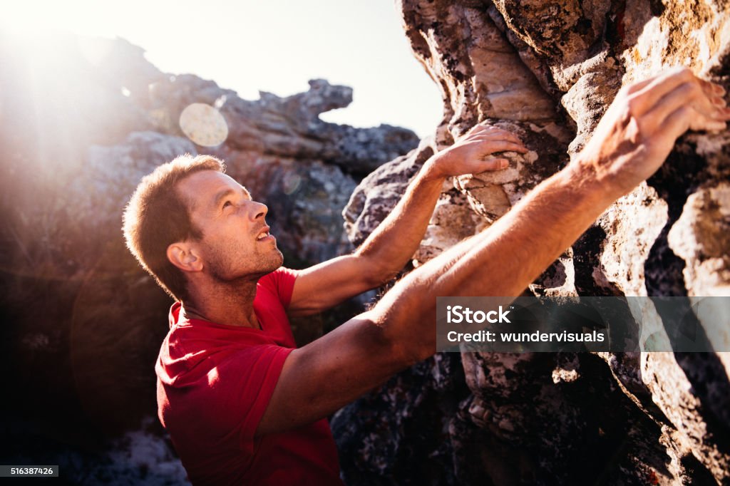 Determination in rock climbing man's face during ascent of mountain Determination and focus showing in rock climbing man's face. He is holding on grip with strong hands and ready to conquer ascent as extreme challenge. Men Stock Photo