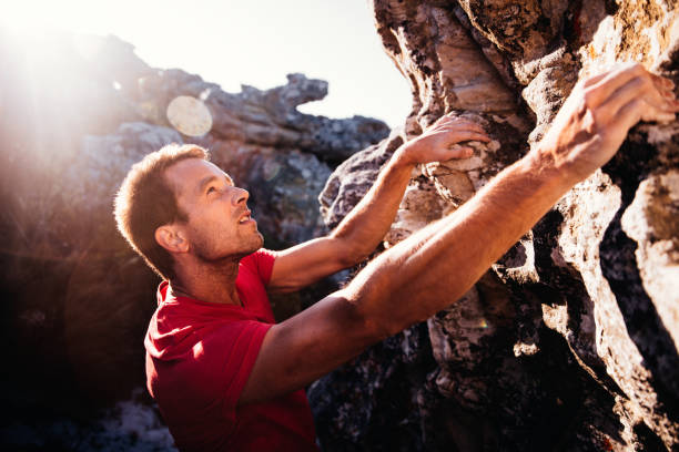 Determination in rock climbing man's face during ascent of mountain Determination and focus showing in rock climbing man's face. He is holding on grip with strong hands and ready to conquer ascent as extreme challenge. rock face stock pictures, royalty-free photos & images