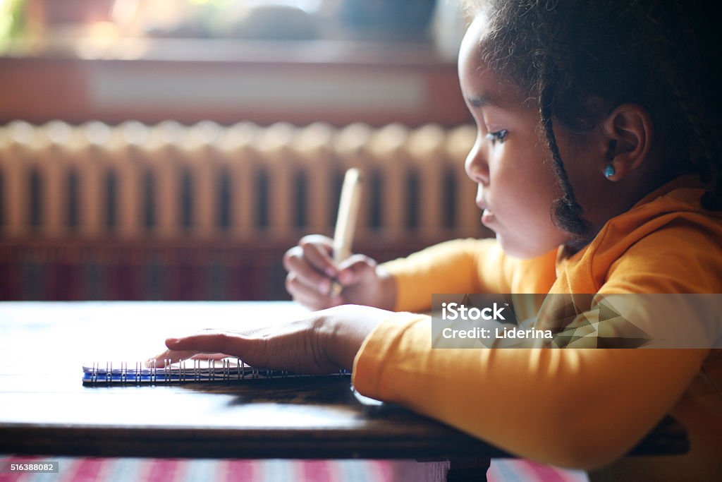 Writing her first book. Profile of little African girl writing  in classroom. Child Stock Photo