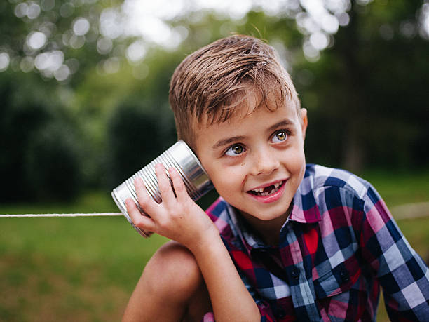 озорная мальчик прослушивания на телефон из консервных банок в руках - telephone can communication tin can phone стоковые фото и изображения