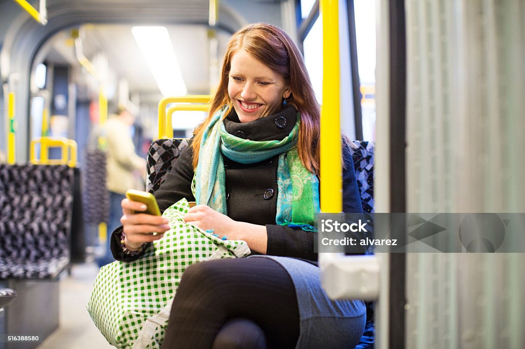 Happy young traveling by subway train using mobile phone Happy young woman texting on her smart phone in public transportation. Female commuter traveling by subway train. City Life Stock Photo