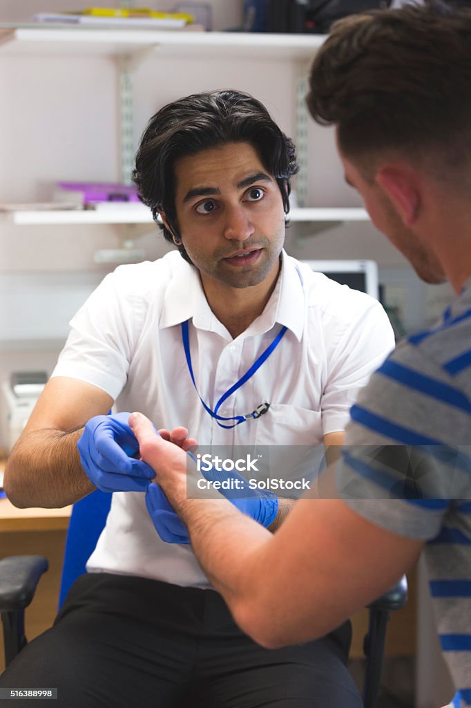 Does this hurt? A close up shot of an Indian doctor examining a male patients wrist and hand. He looks serious and is asking questions about the man's injury, trying to get to the bottom of the problem. They are both sitting in a typically British doctor's office. General Practitioner Stock Photo