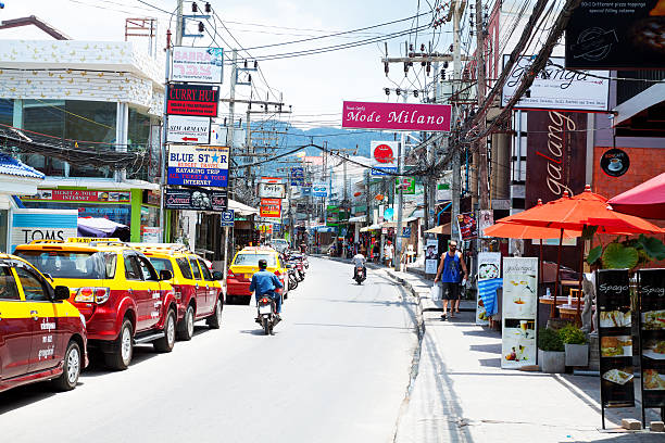 Chaweng, Thailand - May 11, 2014: View along main street in Chaweng. In street are many taxis parked. Some motorcycles are driving in street. In street are many shops, bars and restaurants. OIn sidewalk tourists are walking.