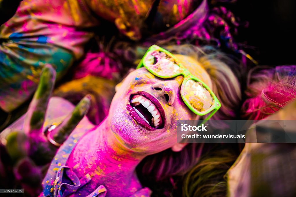 Close up Face Shot of Girl Covered in Holi Powder Close Up face shot of girl covered in colorful powder smiling and making peace sign while laying down on grass in a park during Holi Festival Holi Stock Photo