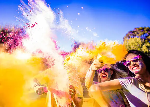 Multi-Ethnic Group of Friends celebrate the holi festival, covered in vibrant colors, smiling and throwing colorful powder at one another