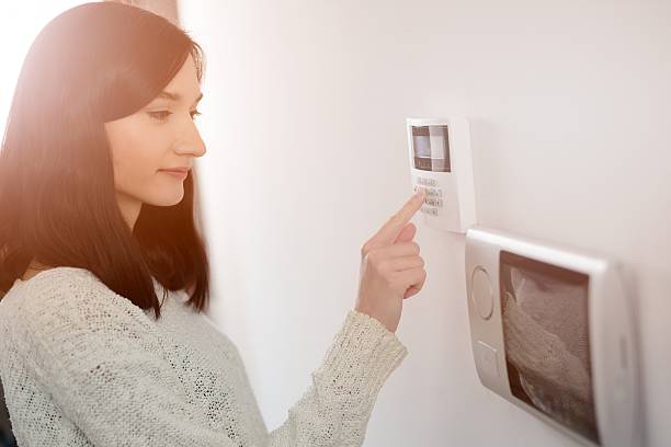 woman entering code on keypad of home security alarm Young brunette woman entering code on keypad of home security alarm. Video intercom next to alarm keypad. fire alarm photos stock pictures, royalty-free photos & images
