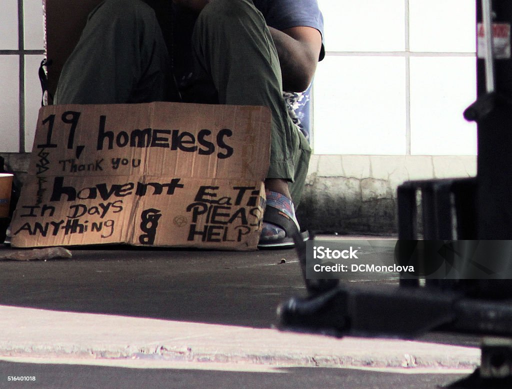 Homeless Teenager Homeless black teenager sits on sidewalk with cardboard sign begging for food and help. Homelessness Stock Photo