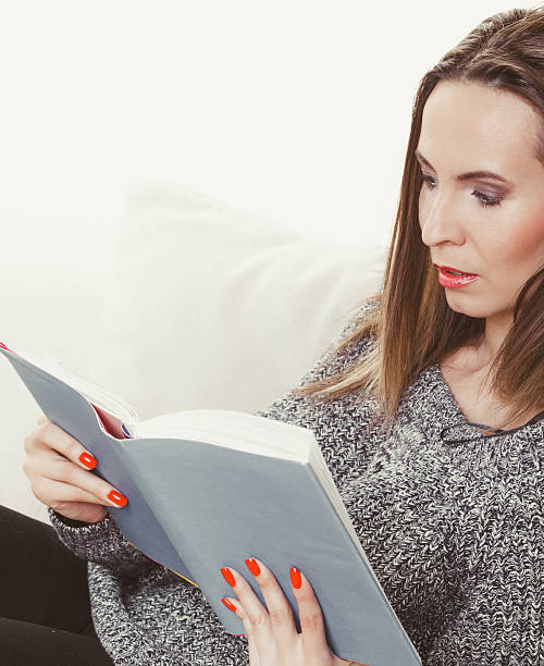 istock Woman sitting on couch reading book at home 516401756