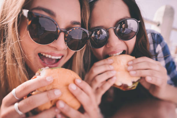 stile retrò di un adolescente ragazza mangia hamburger migliori amici - food people close up outdoors foto e immagini stock