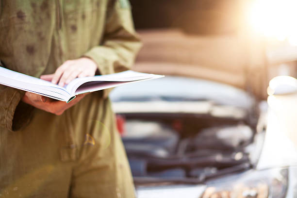 Mechanic reading instructions under open hood Mechanic reading instructions manual and replacing broken part instruction manual photos stock pictures, royalty-free photos & images
