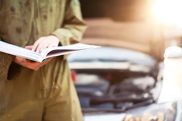 Photo of Mechanic reading instructions under open hood