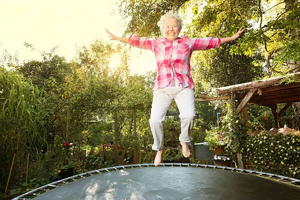 senior woman, 60 yeas old, with overweight, but enjoying to jump on trampoline in garden