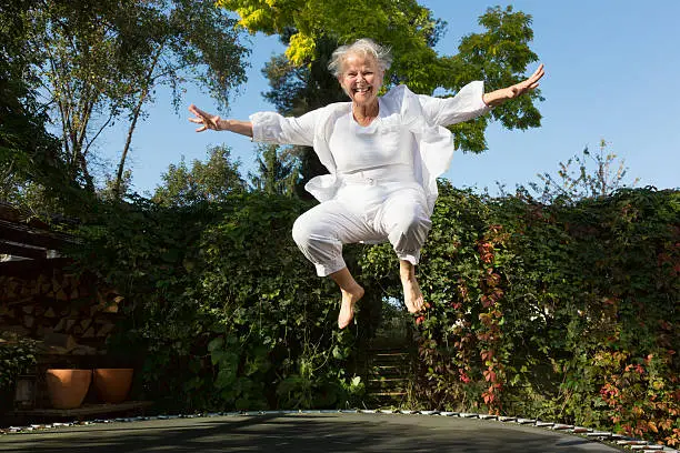 senior woman, 60 yeas old, with overweight, but enjoying to jump on trampoline in garden