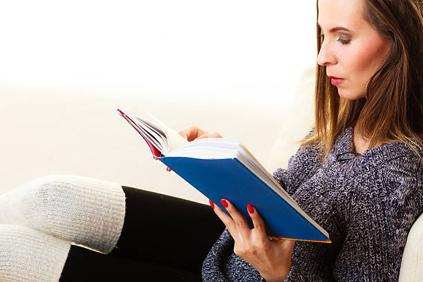 istock Woman sitting on couch reading book at home 516414110