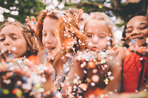Creative shot of a blurred colourful pieces of paper confetti being blown towards the camera on a sunny day by a group of children outdoors