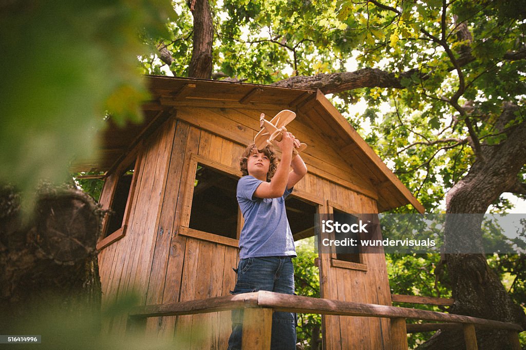 Boy in a treehouse daydreaming with his toy wooden plane Young boy daydreaming while playing with a wooden toy plane in a tree house Tree House Stock Photo