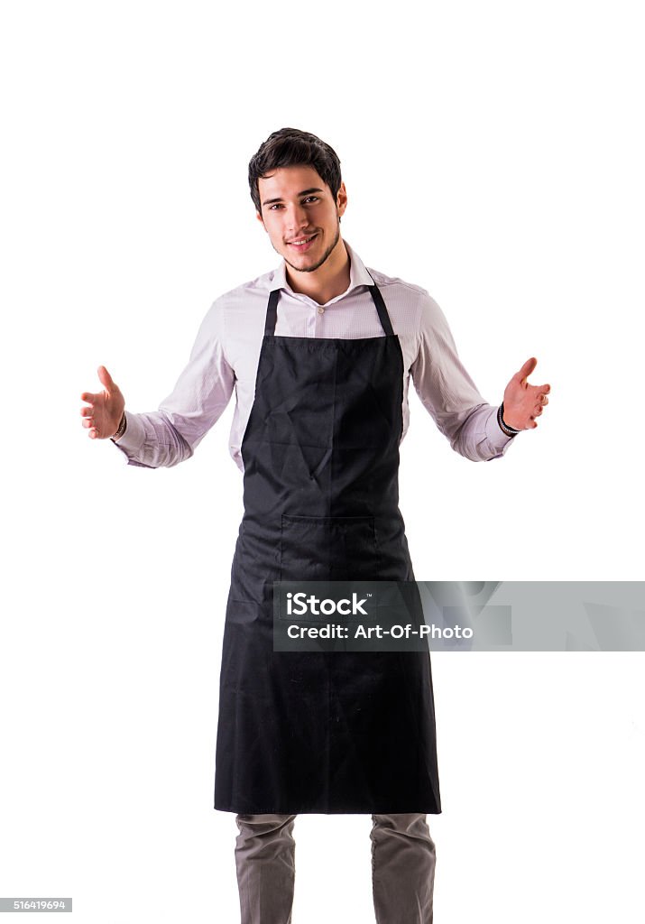 Young chef or waiter wearing black apron isolated Young chef or waiter posing, wearing black apron and shirt isolated on white background, holding empty space between hands Chef Stock Photo