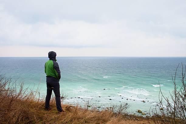 istock Man in green windcheater stand on cliff above bay 516423394