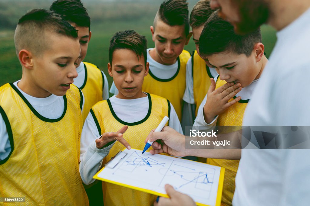 Coach Giving Instruction To His Kids Soccer Team Children playing soccer. Group is standing and coach giving them instructions for new strategy. Trainer is sketching on notepad new strategy. They are having training with their coach on foggy, cold, winter morning. They are dedicated to become a new soccer stars. Soccer Stock Photo
