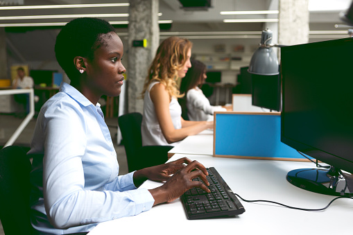 Group of businesswomen working at call center. Selective focus on african female in front using computer.