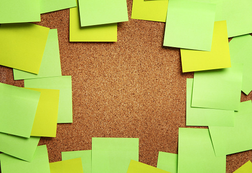 Image of blank green and yellow sticky notes on cork bulletin board with copyspace in the middle