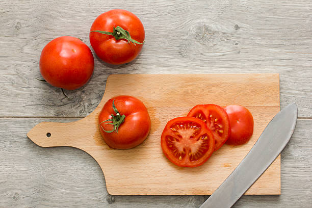 A Close up vivd image of tomato slices on a bamboo cutting board.  The tip of the Chef's knife used to slice the tomato is visible.
