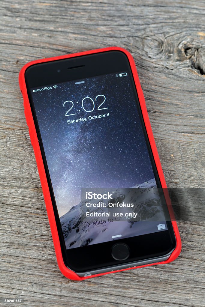 Apple iPhone 6 Inside Red Case Isolated on Wood Background Montreal, Сanada - October 4, 2014: The new Apple iPhone 6, Apples newest version of this revolutionary mobile device displaying the locked screen. Apple Computers Stock Photo